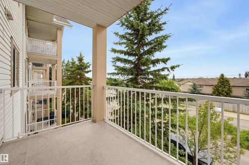 Balcony with textured flooring and white metal railing, offering tree-lined surroundings - #314 245 Edwards Dr Sw, Edmonton, AB - Outdoor With Exterior