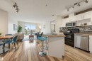 Open-concept living space featuring wood-finish flooring, a kitchen island with seating, white cabinetry, stainless steel appliances, and a glass sliding door opening to a balcony - #314 245 Edwards Dr Sw, Edmonton, AB  - Indoor Photo Showing Kitchen With Stainless Steel Kitchen 