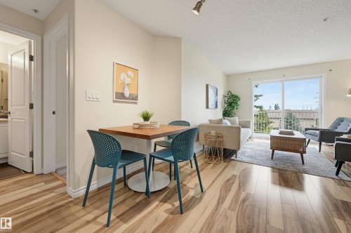 Open-concept living space featuring wood-finish flooring, light-toned walls, and a sliding glass door opening to an outdoor balcony - #314 245 Edwards Dr Sw, Edmonton, AB - Indoor