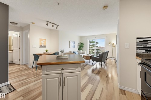 Open-concept living space featuring wood-finish flooring, a sliding glass door leading to a balcony, track lighting, and a kitchen island with a wood countertop - #314 245 Edwards Dr Sw, Edmonton, AB - Indoor