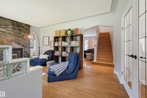 Hardwood flooring, natural stone fireplace surround, built-in shelving, glass block partition, and wood staircase - 10726 128 Street Nw, Edmonton, AB 