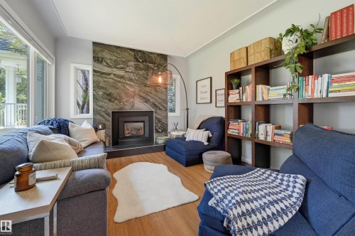 Living area featuring a stone accent wall with a built-in fireplace, wood-finish flooring, large windows, and built-in shelving - 10726 128 Street Nw, Edmonton, AB 