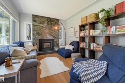 Living area featuring a stone accent wall with a built-in fireplace, wood-finish flooring, large windows, and built-in shelving - 