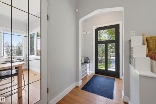 Entryway featuring a black door with glass panels, wood-finish flooring, and a built-in storage bench - 10726 128 Street Nw, Edmonton, AB 