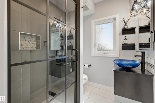 Glass-enclosed shower with black framing, vanity with a vessel sink, black wall-mounted faucet, and overhead cage-style lighting - 10726 128 Street Nw, Edmonton, AB 