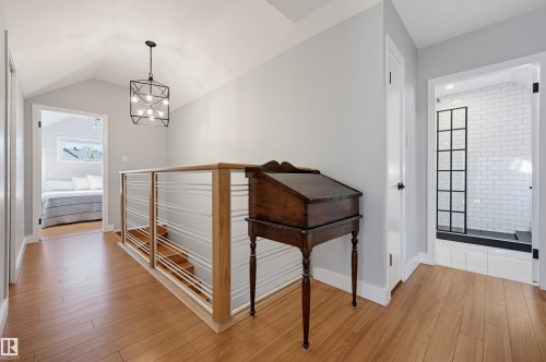 Wood-finish flooring throughout, vaulted ceiling, contemporary chandelier, horizontal cable railing, and a shower with subway tile surround and grid-patterned glass enclosure - 10726 128 Street Nw, Edmonton, AB 