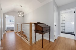 Wood-finish flooring throughout, vaulted ceiling, contemporary chandelier, horizontal cable railing, and a shower with subway tile surround and grid-patterned glass enclosure - 