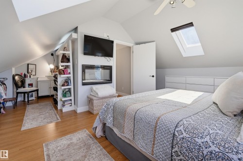 Sloped ceilings with a skylight, wood-finish flooring, built-in shelving, an installed fireplace, and a ceiling fan with integrated lighting - 10726 128 Street Nw, Edmonton, AB 