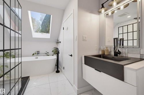 Freestanding soaking tub, skylight, walk-in shower with grid-patterned glass, floating vanity with integrated sink, and wall-mounted faucet - 10726 128 Street Nw, Edmonton, AB 
