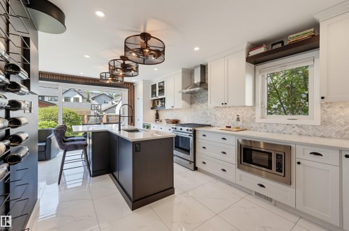 Modern kitchen featuring white shaker cabinetry, stainless steel appliances, a center island with a sink, and a herringbone-patterned backsplash - 10726 128 Street Nw, Edmonton, AB 