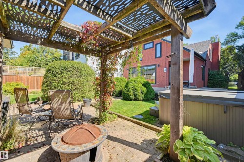 Backyard patio featuring a wood pergola with decorative cutouts, a hot tub, and a brick exterior structure - 10726 128 Street Nw, Edmonton, AB 