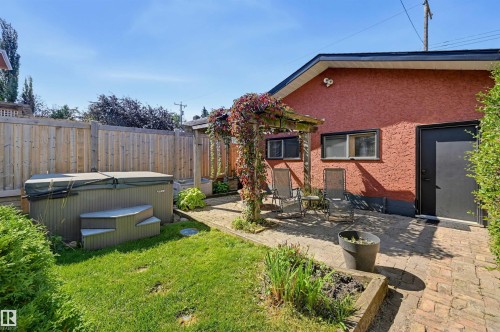 Private yard with a hot tub, wood privacy fence, and a brick paver patio featuring a wood pergola - 10726 128 Street Nw, Edmonton, AB 