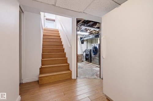 Wood-finish flooring, staircase with wood treads, white painted walls, and an adjacent utility area - 10726 128 Street Nw, Edmonton, AB 