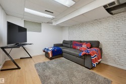 White painted brick accent wall, wood-finish flooring, drop ceiling with integrated lighting, and window with blinds - 