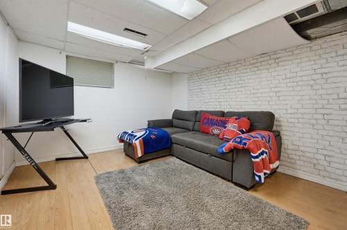 White painted brick accent wall, wood-finish flooring, drop ceiling with integrated lighting, and window with blinds - 10726 128 Street Nw, Edmonton, AB 