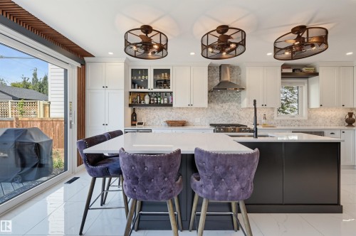 Gourmet kitchen featuring a center island with countertop seating, stainless steel appliances, white cabinetry, and a full-height tile backsplash - 10726 128 Street Nw, Edmonton, AB 