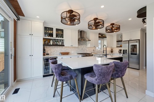 Modern kitchen featuring white shaker cabinetry, an expansive center island with a white countertop, three decorative ceiling fans, and stainless steel appliances - 10726 128 Street Nw, Edmonton, AB 