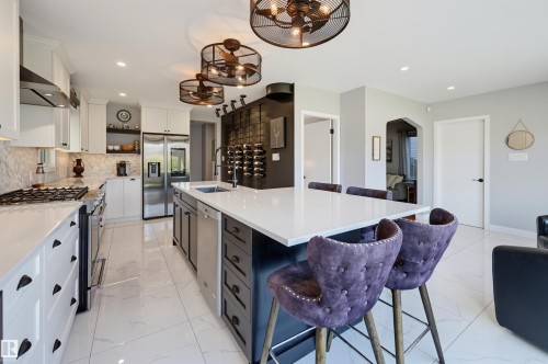 Gourmet kitchen with a large central island, white cabinetry, integrated stainless steel appliances, and tile flooring - 10726 128 Street Nw, Edmonton, AB 