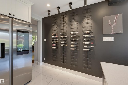 Stainless steel refrigerator, built-in wall-mounted wine racks, track lighting, white baseboards, and white tile flooring - 10726 128 Street Nw, Edmonton, AB 