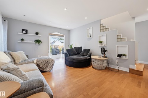 Recessed lighting illuminates the open living area featuring wood-finish flooring, built-in shelving, and a stepped wall with integrated glass block accents - 10726 128 Street Nw, Edmonton, AB 