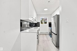 White cabinetry with black hardware, black marble-patterned backsplash, white countertops, stainless steel appliances, and light wood-finish flooring - 
