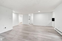 Light wood-finish flooring throughout, white walls, recessed ceiling lighting, white baseboards, and built-in white cabinetry with a dark backsplash - 