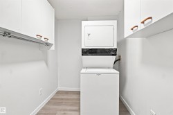 Laundry area with stackable appliances, wood-finish flooring, and white cabinetry featuring wood pulls - 