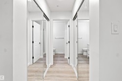 Light wood-finish flooring, white walls, and mirrored closet doors - 
