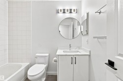 White tiled shower with a bathtub, white vanity with an integrated sink, and a circular mirror - 