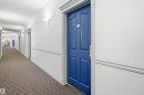 Hallway featuring textured white walls, decorative wall molding, patterned carpet flooring, and sconce lighting - #124 10511 42 Av Nw, Edmonton, AB 