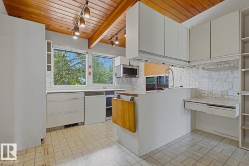 Kitchen featuring a wood-panel vaulted ceiling, white cabinetry, light-toned tile flooring, built-in microwave, and integrated desk space - 7508 139 Street Nw, Edmonton, AB 