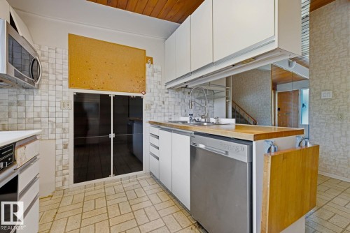 Kitchen featuring a stainless steel dishwasher, stainless steel sink, wood-finish countertop, white cabinetry, and tile flooring - 7508 139 Street Nw, Edmonton, AB 