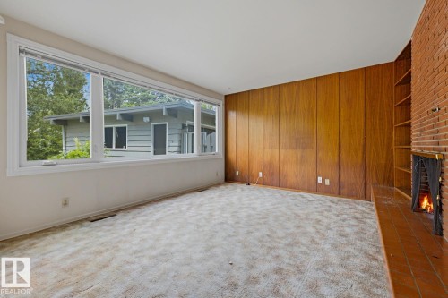 Expansive windows, brick fireplace with tile hearth, wood paneling, and built-in shelving - 7508 139 Street Nw, Edmonton, AB 