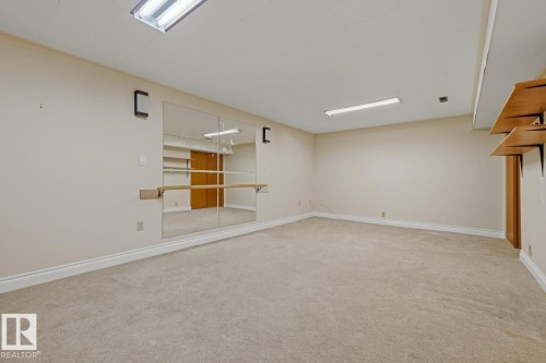 Carpeted room featuring a mirrored wall with a wooden ballet barre and track lighting - 7508 139 Street Nw, Edmonton, AB 