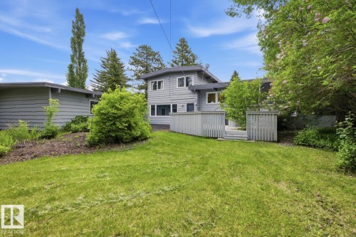 Expansive green lawn with mature landscaping, a private wooden deck, and a multi-level exterior - 7508 139 Street Nw, Edmonton, AB 