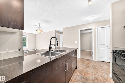 Kitchen island with double basin sink, dark cabinetry, and a gooseneck faucet - #218 5810 Mullen Pl Nw Nw, Edmonton, AB 