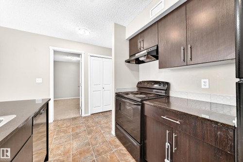 Kitchen featuring dark wood-finish cabinetry, solid surface countertops, a black electric range, and tile flooring - #218 5810 Mullen Pl Nw Nw, Edmonton, AB 