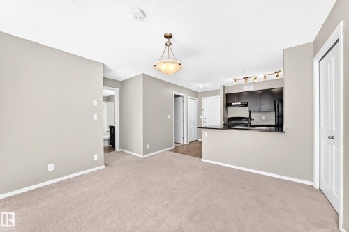 Neutral-toned carpet flooring, light gray wall paint, and a bronze-finish chandelier - #218 5810 Mullen Pl Nw Nw, Edmonton, AB 