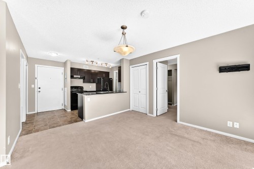 Kitchen featuring dark wood-finish cabinetry, black appliances, and a breakfast bar - #218 5810 Mullen Pl Nw Nw, Edmonton, AB 