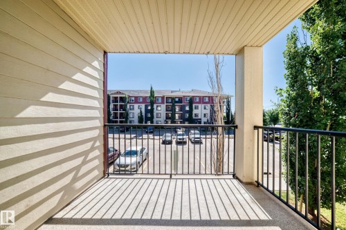 Balcony with black metal railing, concrete flooring, and slatted ceiling - #218 5810 Mullen Pl Nw Nw, Edmonton, AB 