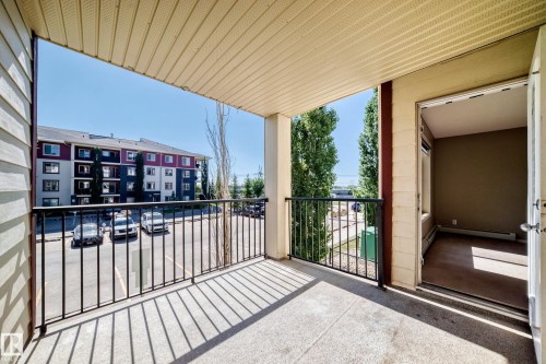 Balcony with concrete flooring and black metal railing, featuring a panel-style ceiling - #218 5810 Mullen Pl Nw Nw, Edmonton, AB 