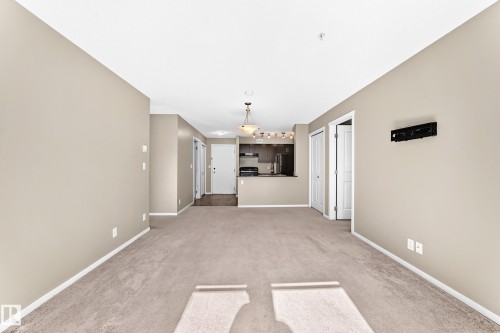 Bright living area with neutral carpeting, light neutral walls, and white trim - #218 5810 Mullen Pl Nw Nw, Edmonton, AB 