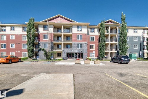 Multi-story building featuring balconies, a prominent entrance, and a parking area - #218 5810 Mullen Pl Nw Nw, Edmonton, AB 