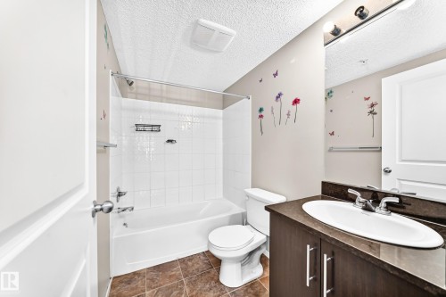 Bathtub with white subway tile surround, complementing a dark wood-finish vanity with an integrated sink and chrome fixtures - #218 5810 Mullen Pl Nw Nw, Edmonton, AB 