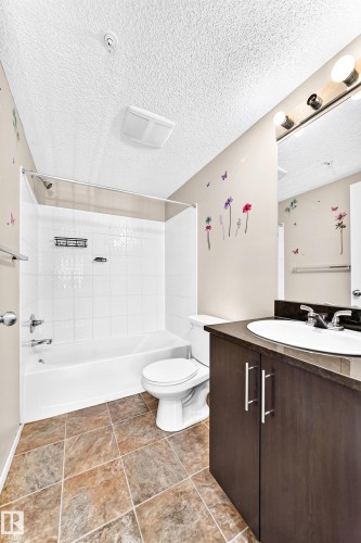 Tile flooring, white subway tile shower surround, shower/tub combination, dark wood-finish vanity, and a white basin sink - #218 5810 Mullen Pl Nw Nw, Edmonton, AB 