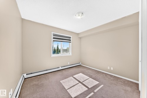 Neutral-toned walls, carpeted flooring, and a single window with blinds - #218 5810 Mullen Pl Nw Nw, Edmonton, AB 