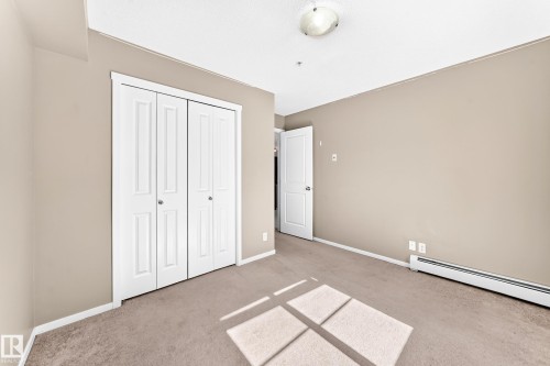 Neutral tone painted walls, white trim, carpeted flooring, built-in closet with bi-fold doors, and a flush mount ceiling light - #218 5810 Mullen Pl Nw Nw, Edmonton, AB 
