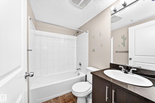 White tiled tub and shower combination with a curved shower rod - #218 5810 Mullen Pl Nw Nw, Edmonton, AB 