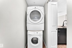 Stacked washer and dryer unit with a paneled door, black cabinetry, and a gooseneck faucet - 
