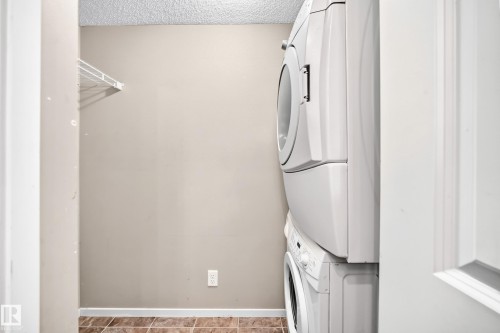 Laundry area featuring a stacked washer and dryer, wire shelving, and tiled flooring - #218 5810 Mullen Pl Nw Nw, Edmonton, AB 
